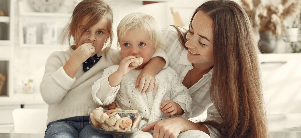 Mother and kids enjoying cookies in a warm, cozy kitchen setting.