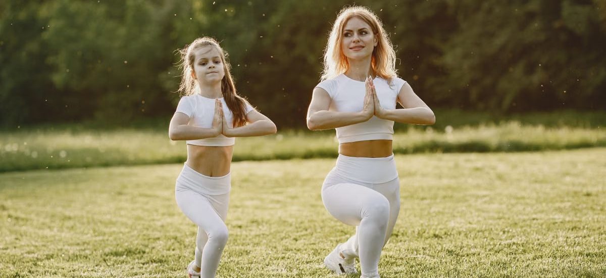 A mother and daughter practicing yoga together in matching outfits in a sunny park.
