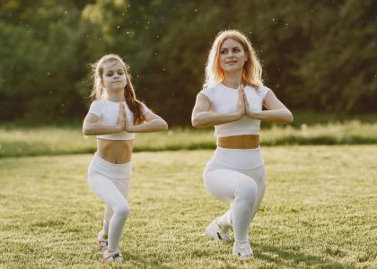A mother and daughter practicing yoga together in matching outfits in a sunny park.